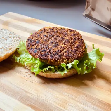 Una hamburguesa vegana de lentejas abierta, se ve el pan, la lechuga y la torta sin adiciones.